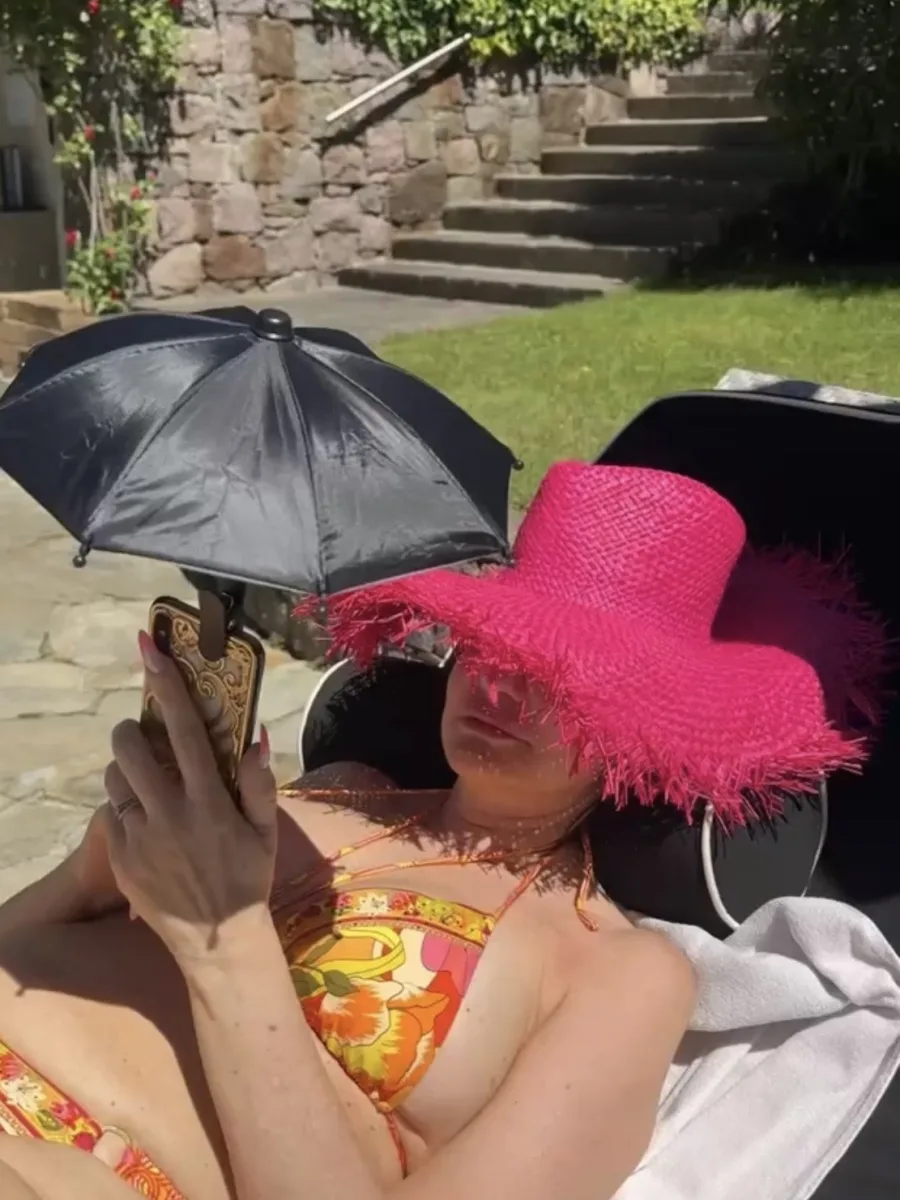 Michaela sitzt am Pool und hält ein Smartphone mit angeklipptem schwarzem Mini-Sonnenschirm