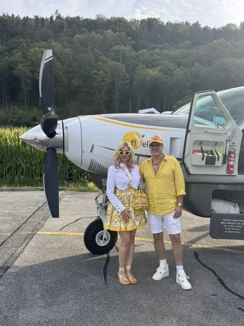Michi und Silvio stehen in gelb-weißen Sommerlooks vor dem Flugzeug