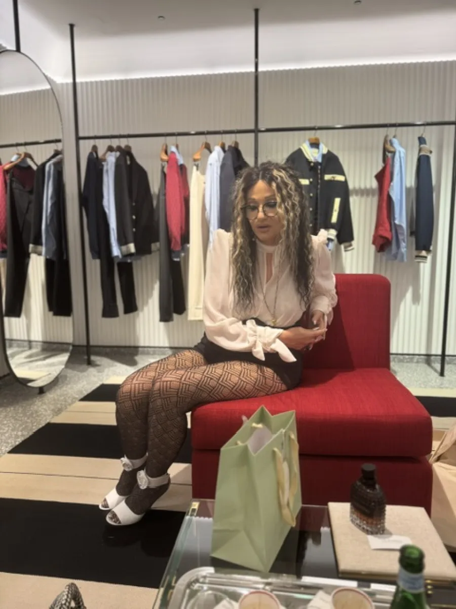 Michaela Hoppe sitzt in einer Boutique und trägt gemusterte Strumpfhosen zu weißen offenen Schuhen