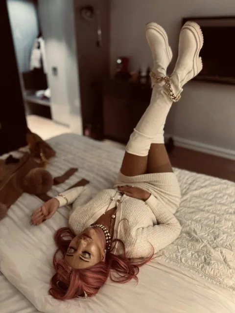 Michaela liegt entspannt in einem weißen Outfit und weißen Stiefeln auf einem Hotelbett