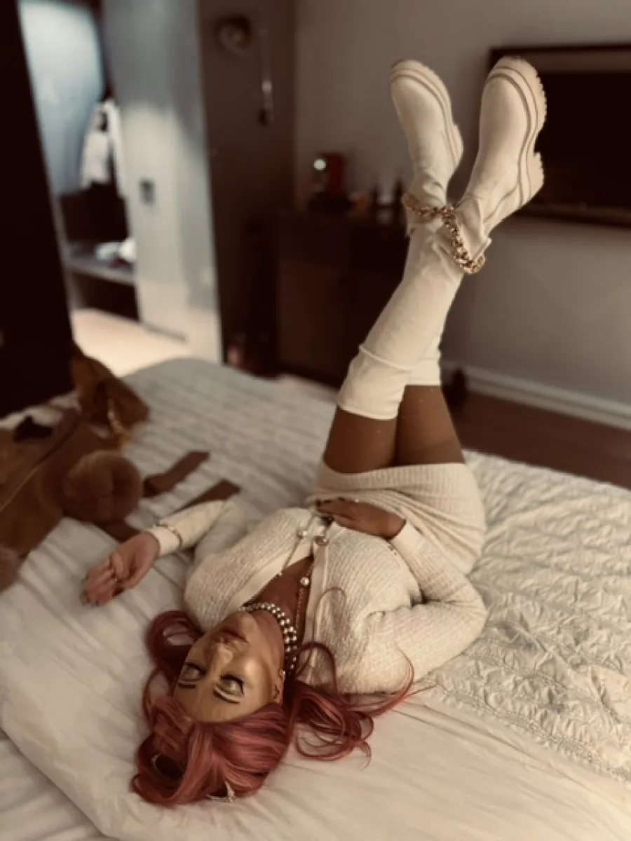 Michaela liegt entspannt in einem weißen Outfit und weißen Stiefeln auf einem Hotelbett