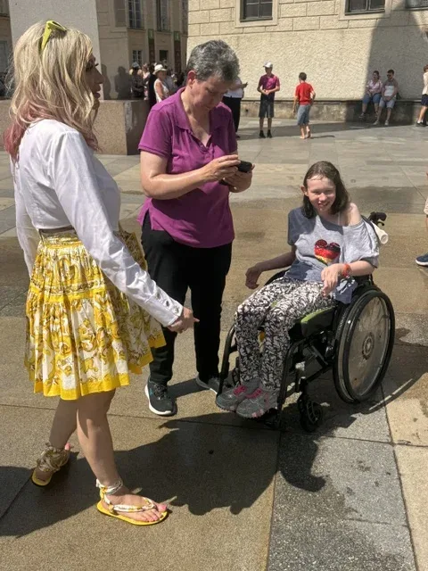 Michi und eine Begleiterin stehen bei Sarah im Rollstuhl auf einem Platz in Prag