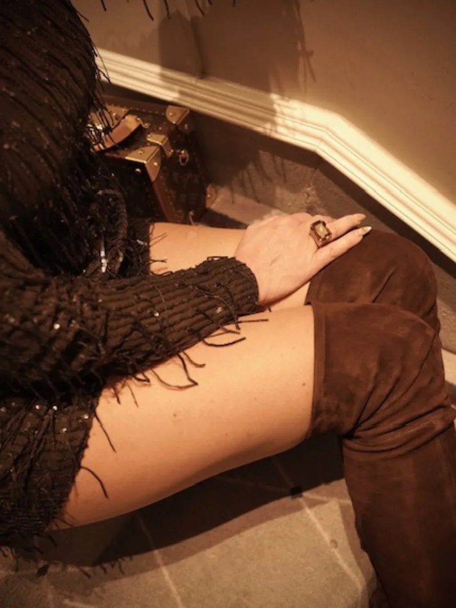 Detailaufnahme von schwarzem Paillettenkleid, Ring und braunem Overknee-Stiefel