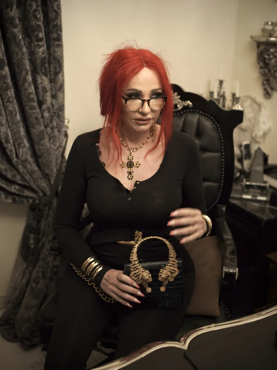 Michaela Hoppe in schwarzem Outfit mit goldenen Accessoires und einer markanten Tigertasche am Schreibtisch