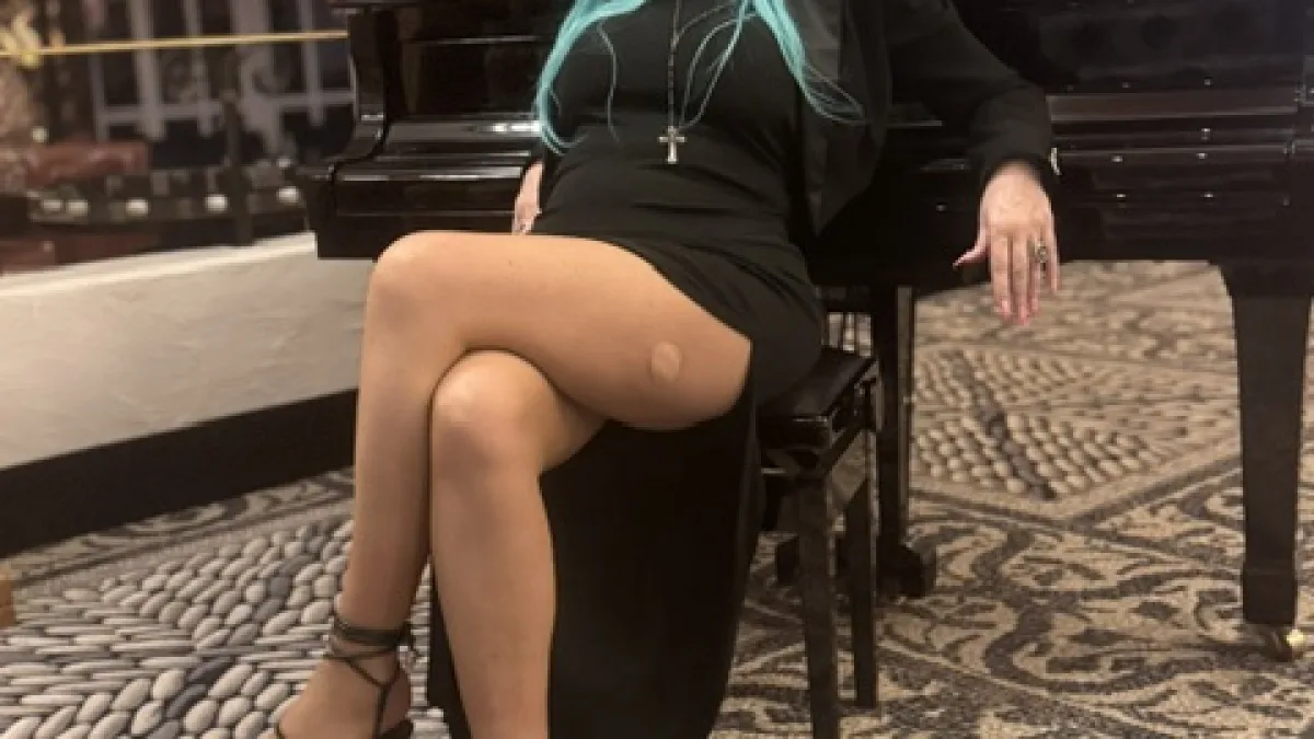 Michaela Hoppe in schwarzem Kleid mit feiner Strumpfhose und offenen Sandaletten an einem Flügel