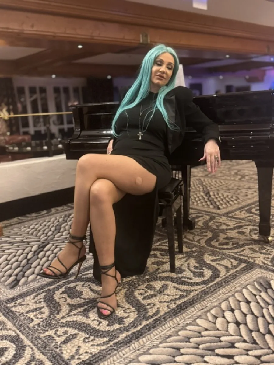 Michaela vollständig in schwarzem Kleid mit feiner Strumpfhose und offenen Sandaletten an einem Flügel