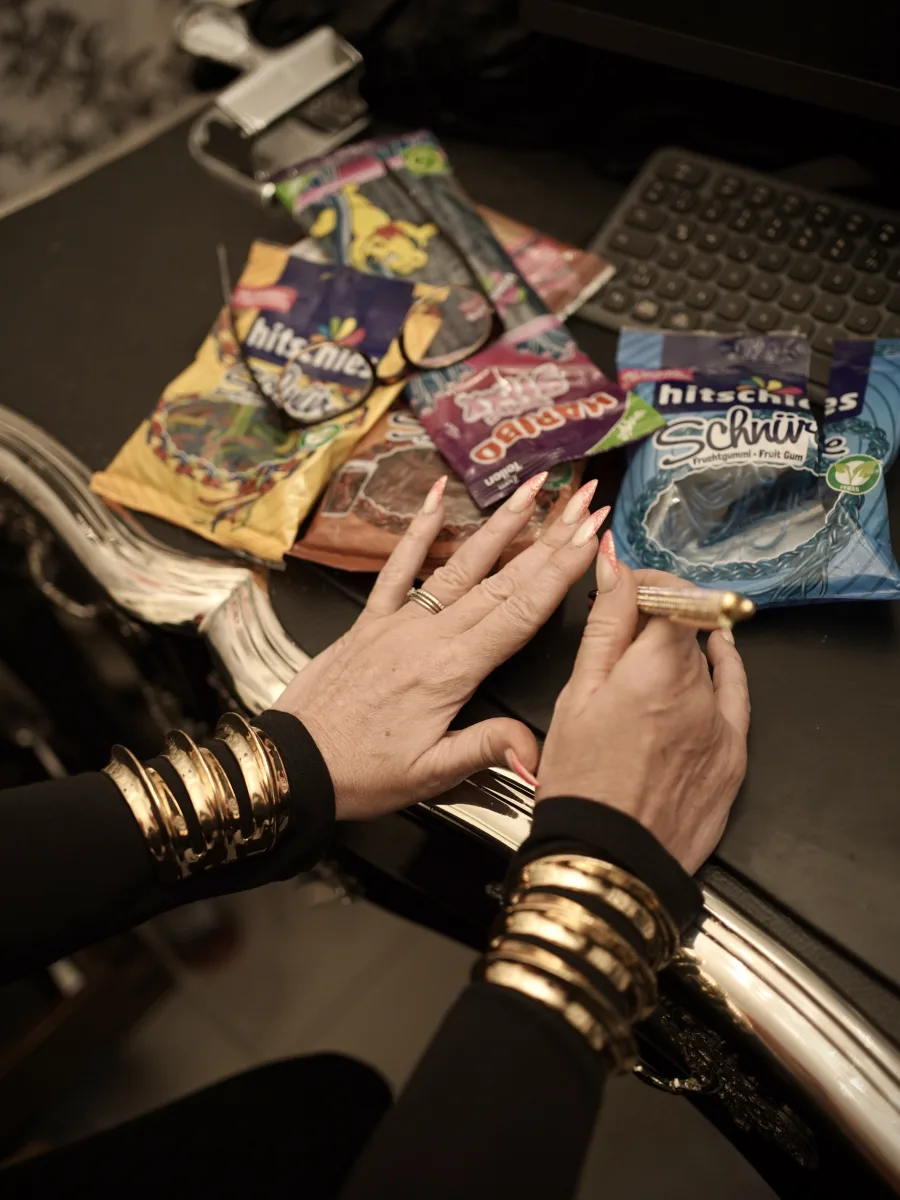 Goldene Armreifen und lange Fingernägel zwischen Fruchtgummi und Tastatur auf dem Schreibtisch