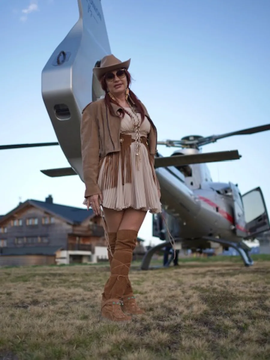Michaela in braunen Overknee-Boots und Fransengürtel vor einem Helikopter
