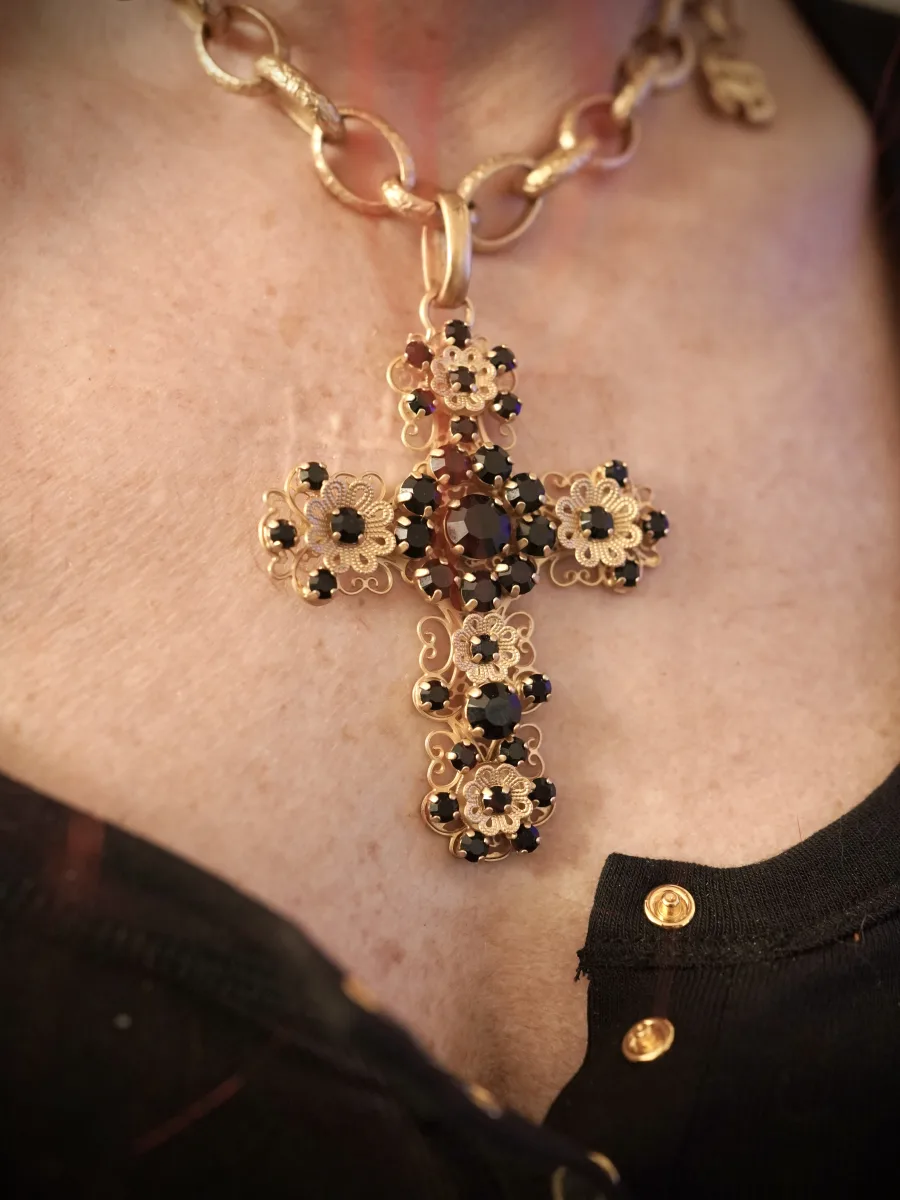 Großes goldenes Kreuz mit dunklen Steinen an einer Gliederkette