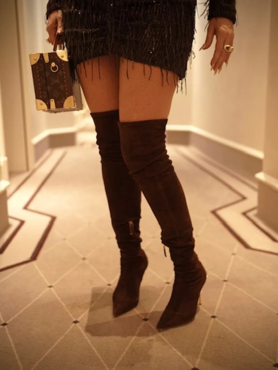 Detailaufnahme von Overknees, Kleid und kleiner Koffertasche im Hotelkorridor